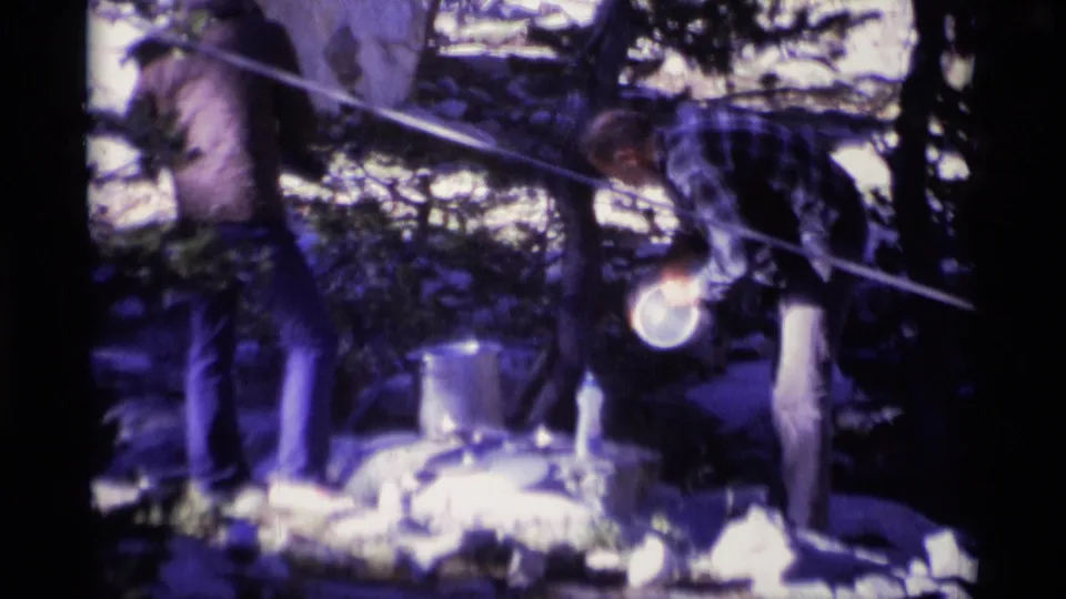 1975 Minaret Wilderness 8mm frame showing two men handling campsite cookware among rocks and pine trees.