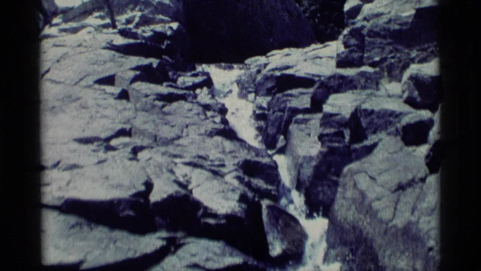 1975 8mm Minaret Wilderness footage showing a narrow stream cascading through gray rocks with dark film borders.