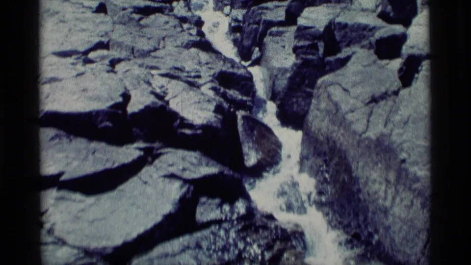 The stream appears in a tighter rocky channel, with white water dropping between gray stones in 1975 California wilderness footage.