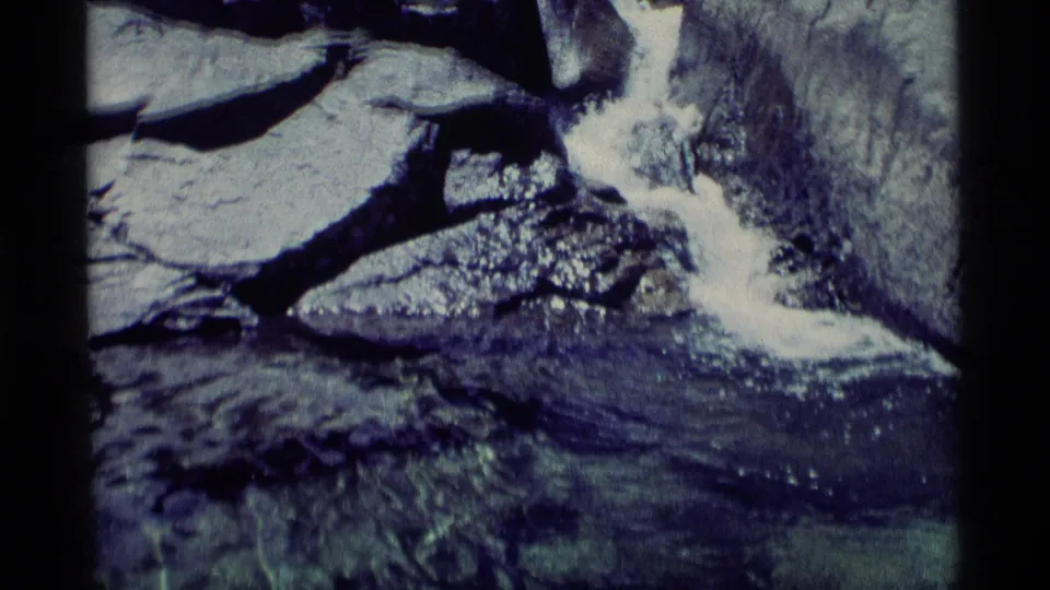 A rocky cascade pours into a shallow pool, with ripples and submerged stones visible in the 8mm frame.