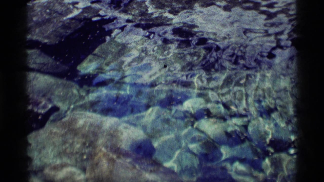 Submerged rocks seen through rippling blue-green water with dark 8mm frame edges.