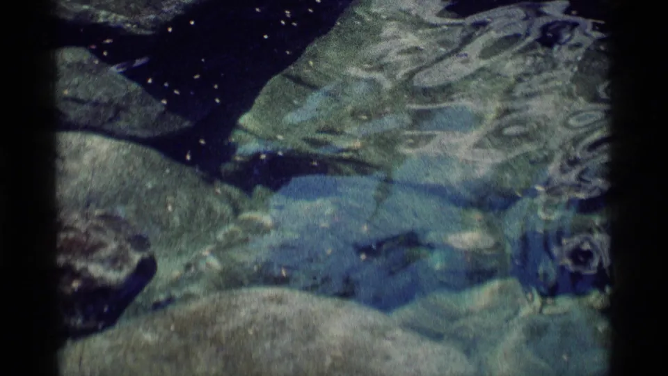 Submerged boulders appear through blue-green water in this 1975 Minaret Wilderness home-movie frame.