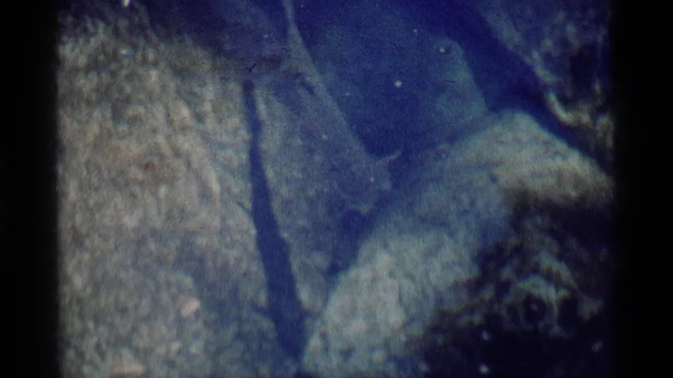 1975 8mm close-up of a fish crossing over submerged rocks in blue-green wilderness water.