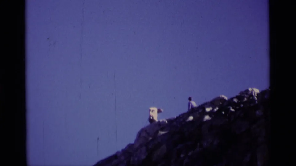 Two hikers stand far apart on a sloped rocky ridge in Minaret Wilderness, recorded on 8mm film in 1975.
