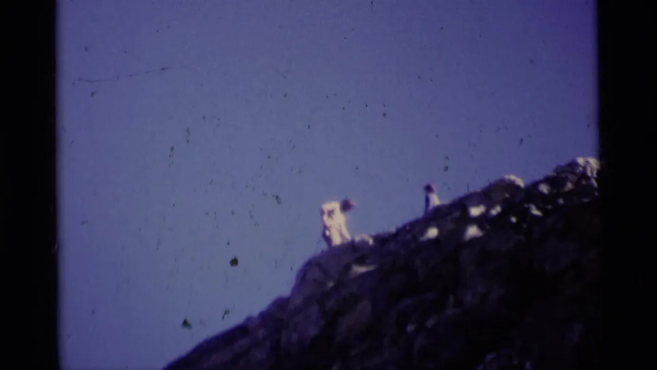The final 1975 8mm frame shows two distant hikers near the crest of a dark rocky ridge in Minaret Wilderness.