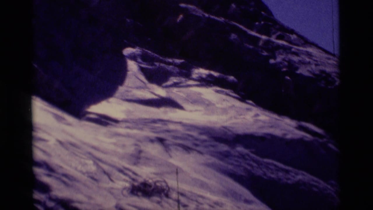 Dark rocky mountainside with pale sloped terrain and black film borders.