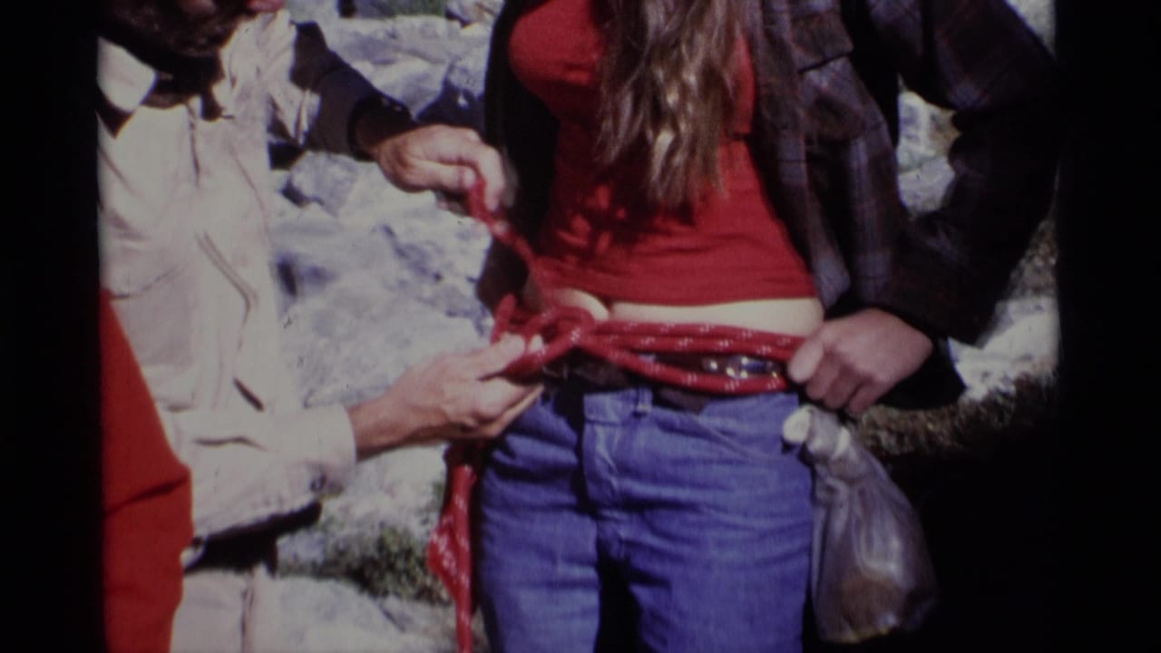 Hands begin wrapping a red rope around a woman's waist over blue jeans.