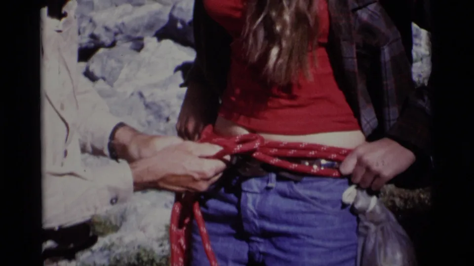 Hands tighten or align the red rope across the front of a woman's jeans in a close outdoor 8mm shot.