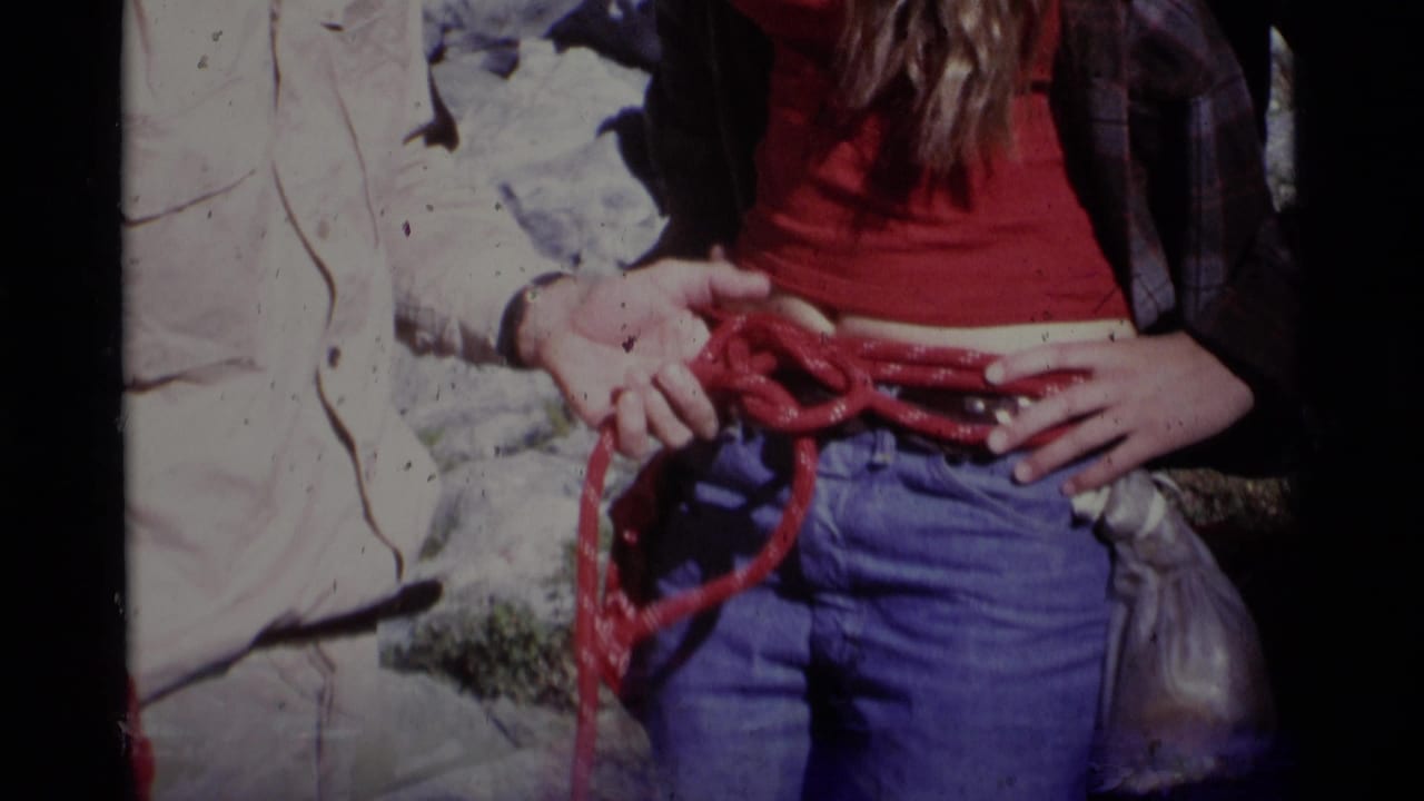 1975 8mm Minaret Wilderness footage showing hands arranging red climbing rope at a climber's waist before a rock climb.