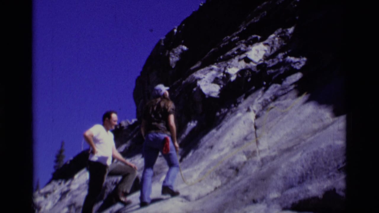 Two adults stand on a sloped granite rock face under a deep blue sky.
