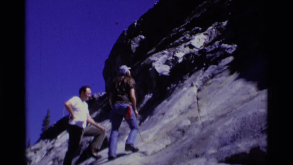Two climbers in the Minaret Wilderness stand on pale granite beneath a dark rock outcrop and deep blue sky.