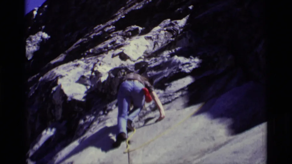 1975 Minaret Wilderness frame showing an adult climber in jeans leaning into a steep gray rock face with rope visible.