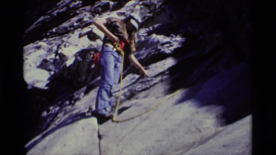 1975 California wilderness frame showing an adult hiker near a rocky ledge, holding position on a steep face with rope visible.