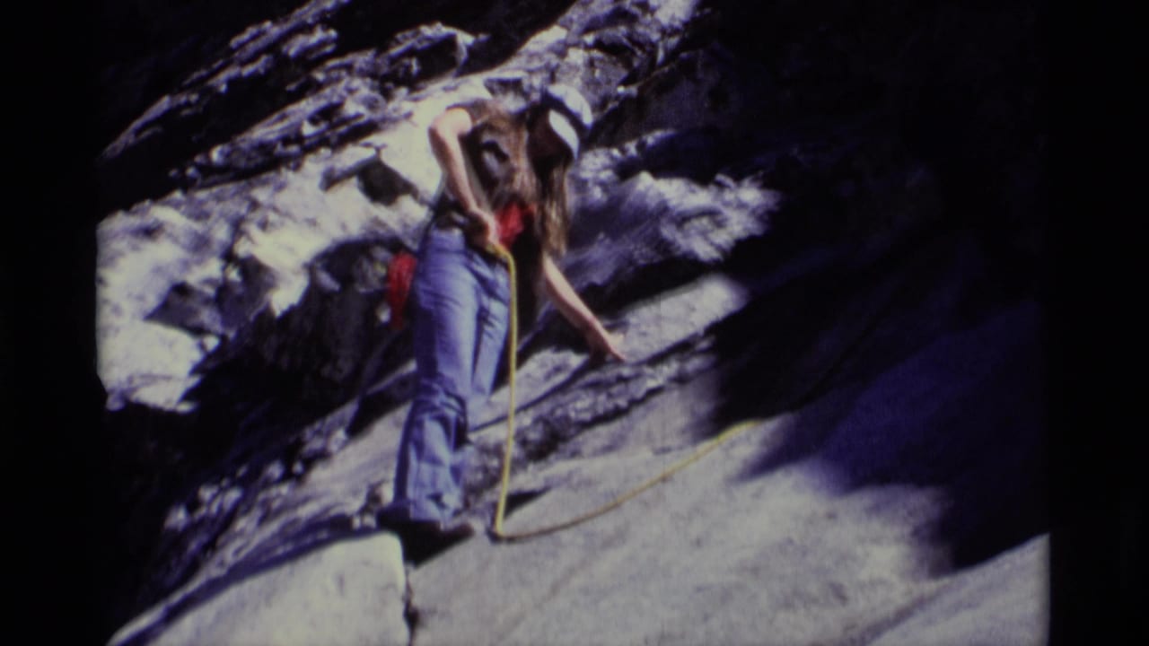 1975 8mm frame from Minaret Wilderness showing a helmeted climber in jeans on a steep rock face with a yellow rope.