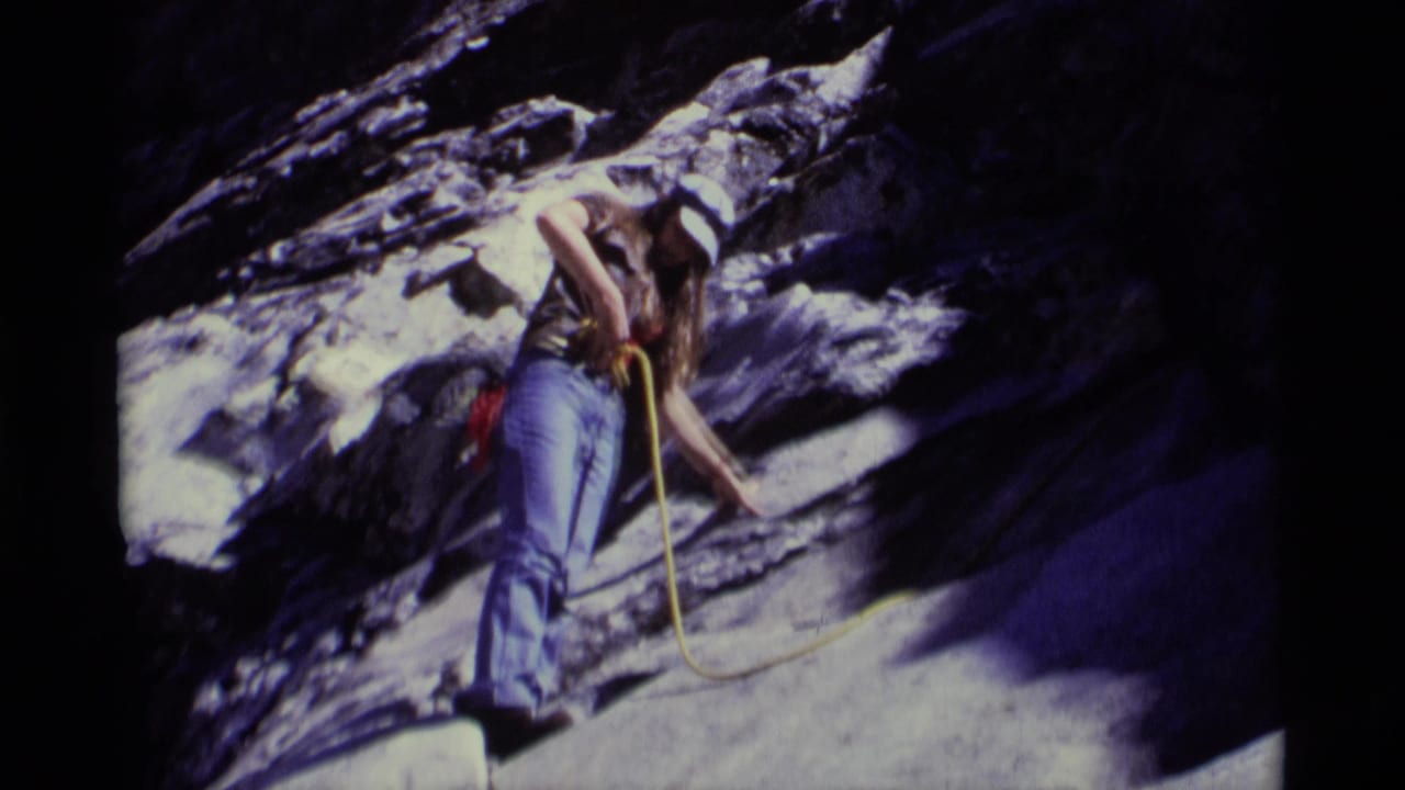 Climber stands against rugged rock with a yellow rope trailing downward.
