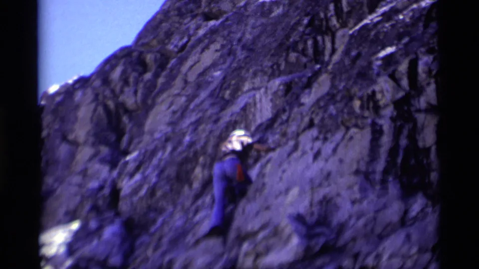 1975 Minaret Wilderness frame with a small helmeted climber ascending against a broad dark rock face.