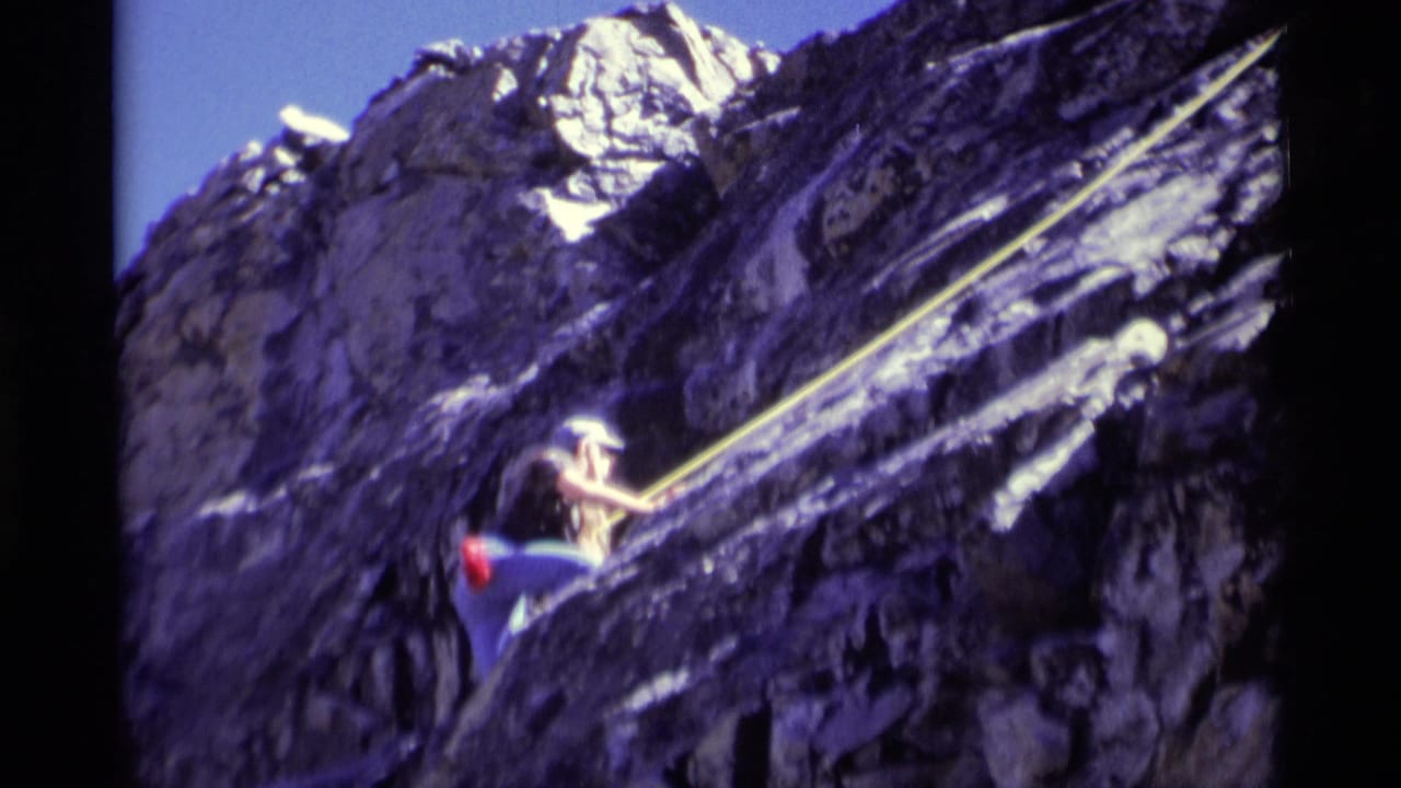 The climber reaches higher on the rugged rock face, with the yellow rope stretched diagonally across the 1975 wilderness frame.