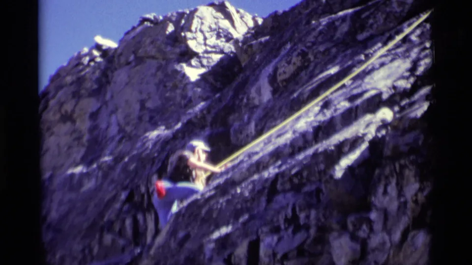 The climber reaches higher on the rugged rock face, with the yellow rope stretched diagonally across the 1975 wilderness frame.