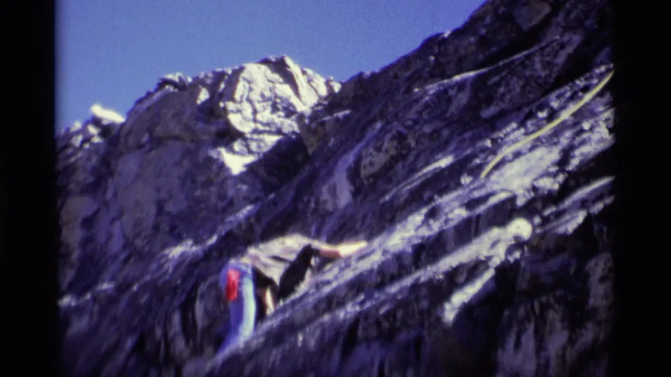 The climber appears partly lower in the frame against the steep, shadowed rock face and blue sky in the 1975 California wilderness clip.