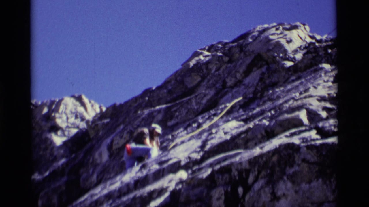 A helmeted climber ascends a steep rock face in Minaret Wilderness, California, in 1975, with rope visible against rugged stone and blue sky.
