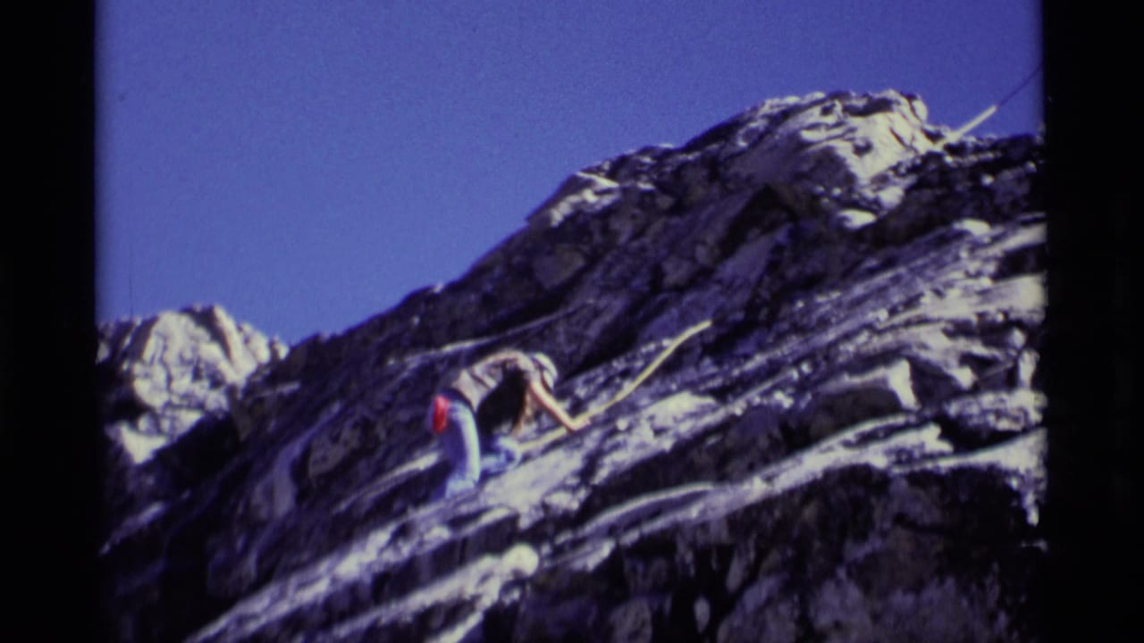 Climber reaches across a sloped rock face with rope nearby.