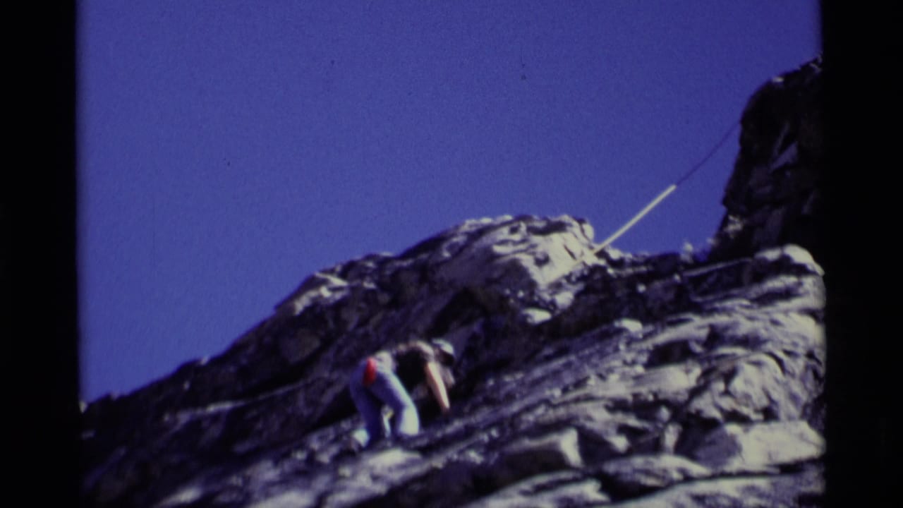 Roped climber crouches on a rocky ledge with rope stretching across the cliff.