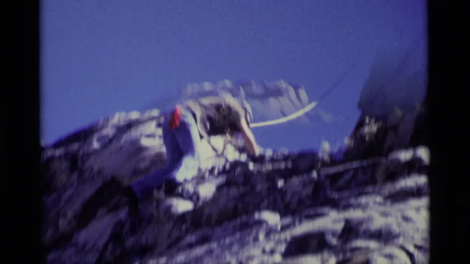Soft 8mm frame from the Minaret Wilderness clip showing the climber leaning forward on rock with a rope visible behind.