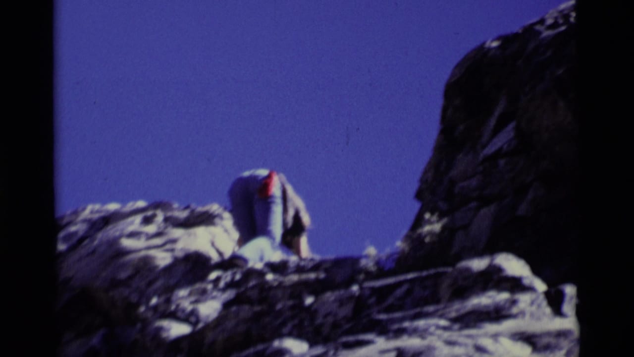 1975 8mm frame from Minaret Wilderness showing a climber on a rocky ledge with rope visible below a deep blue sky.
