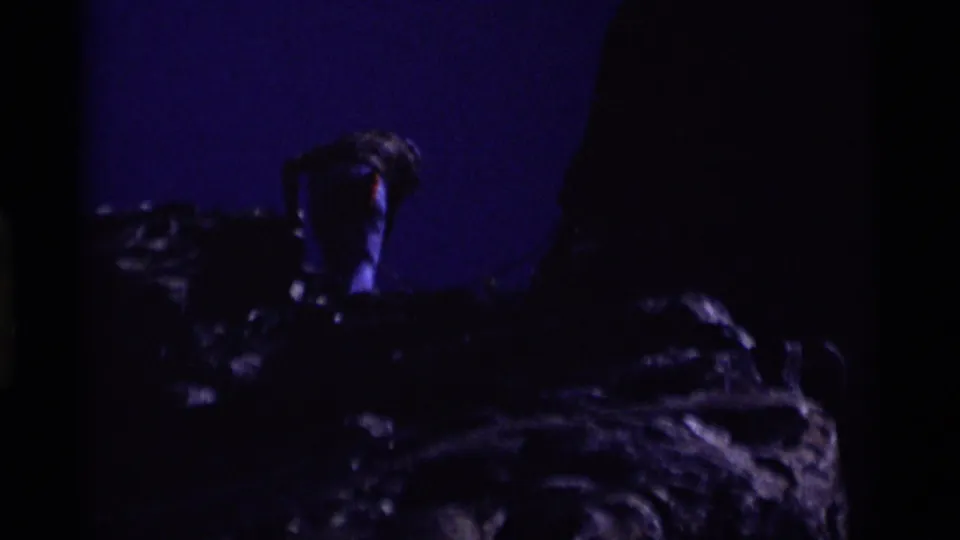 A 1975 8mm frame shows the climber descending into shadow on the rock face, with blue sky still visible at the edge.
