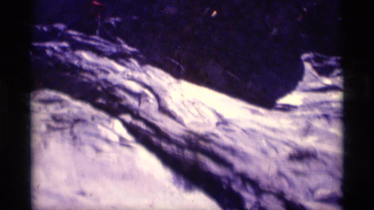 Grainy 1975 8mm frame from Minaret Wilderness showing a pale rocky cliff face under dark shadow and strong purple color shift.