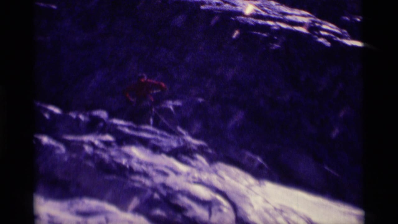 Distant climber in a red shirt appears on a rugged Minaret Wilderness rock slope in purple-shifted 1975 8mm footage.