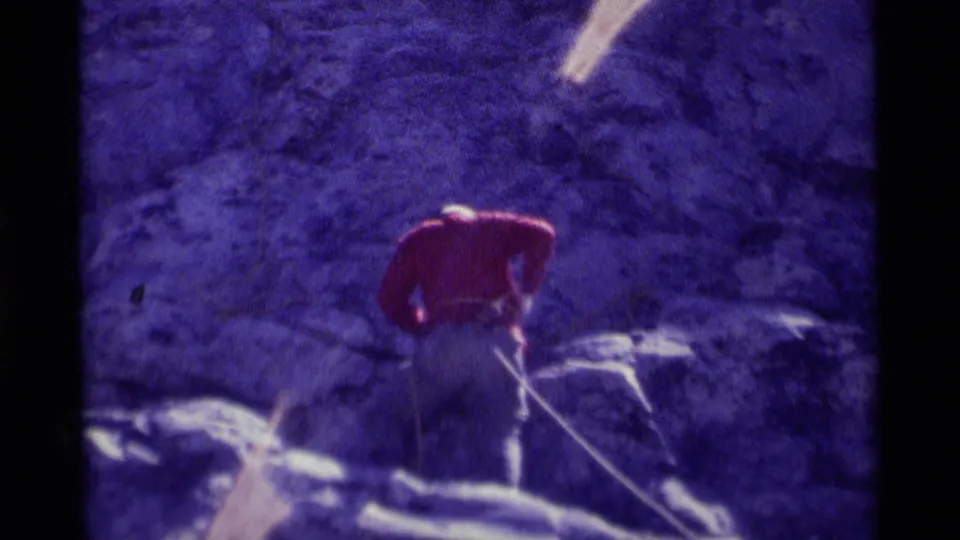 Red-shirted climber remains on the rocky face with rope visible in a grainy 1975 Minaret Wilderness home-movie frame.