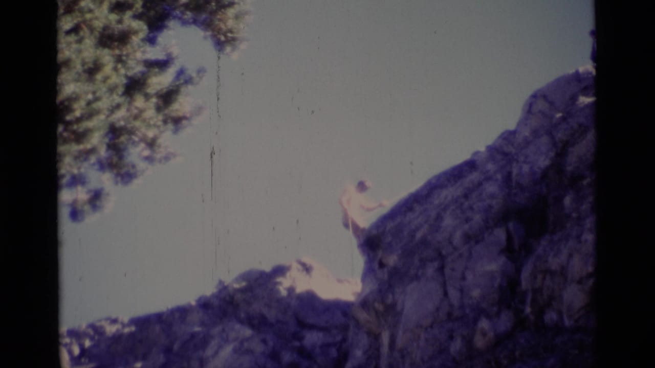 1975 California wilderness footage shows a man at the rim of a rugged cliff, partly silhouetted against open sky.