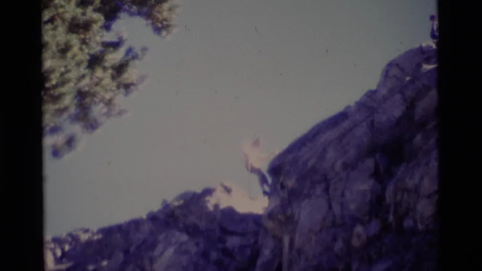 1975 Minaret Wilderness frame showing a man rappelling or climbing down a rugged cliff in handheld 8mm footage.