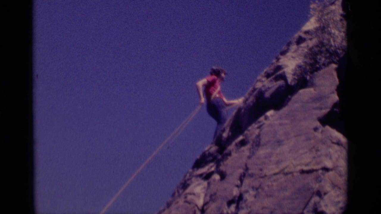 The climber appears near the upper edge of the rocky formation, framed by blue sky in the 1975 Minaret Wilderness footage.