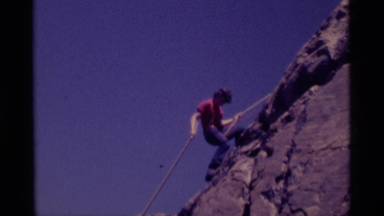 Roped climber moves lower on a rocky cliff with open blue sky behind.