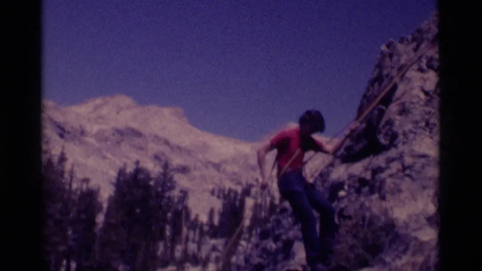 A 1975 Minaret Wilderness frame shows the climber near the lower rock face, with trees and pale mountain terrain behind.