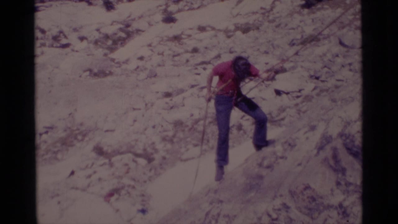 Man in a red shirt moves down a rocky cliff with a rope.