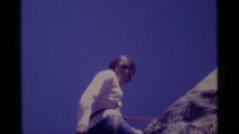 A closer 8mm frame shows the white-shirted climber near the rock face, with a rope crossing the scene against blue sky.