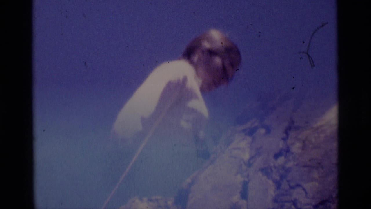 1975 8mm frame in Minaret Wilderness showing a woman leaning forward with rope near a steep rock face.