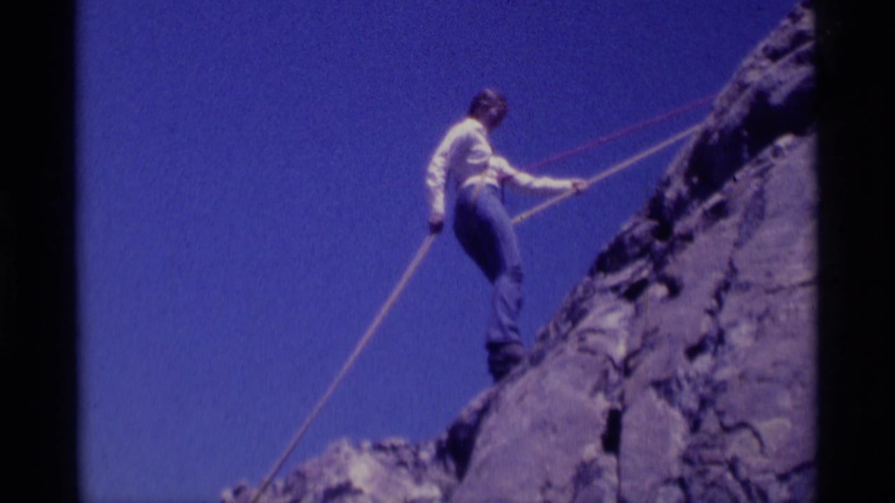 Climber on a steep rocky slope using ropes under a clear blue sky.