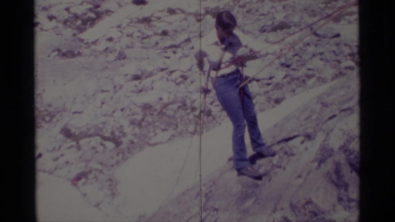 1975 Minaret Wilderness home-movie frame showing a hiker in jeans navigating a pale rocky slope with rope support.