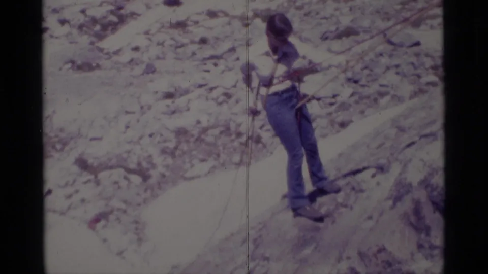1975 Minaret Wilderness home-movie frame showing a hiker in jeans navigating a pale rocky slope with rope support.