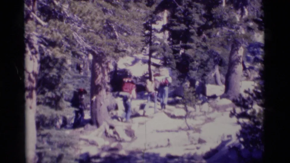 1975 California wilderness frame with hikers near boulders and pine trees, seen in soft 8mm focus.