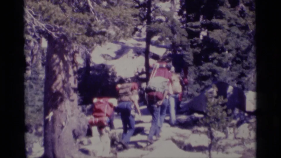 1975 8mm frame of hikers with large packs moving up a snowy forest trail in the Minaret Wilderness area.