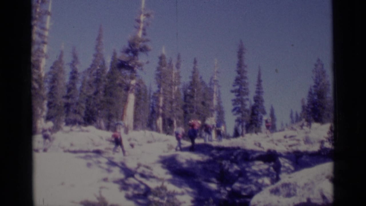 Backpackers appear in a wide snowy forest clearing during a 1975 Minaret Wilderness home-movie scene.