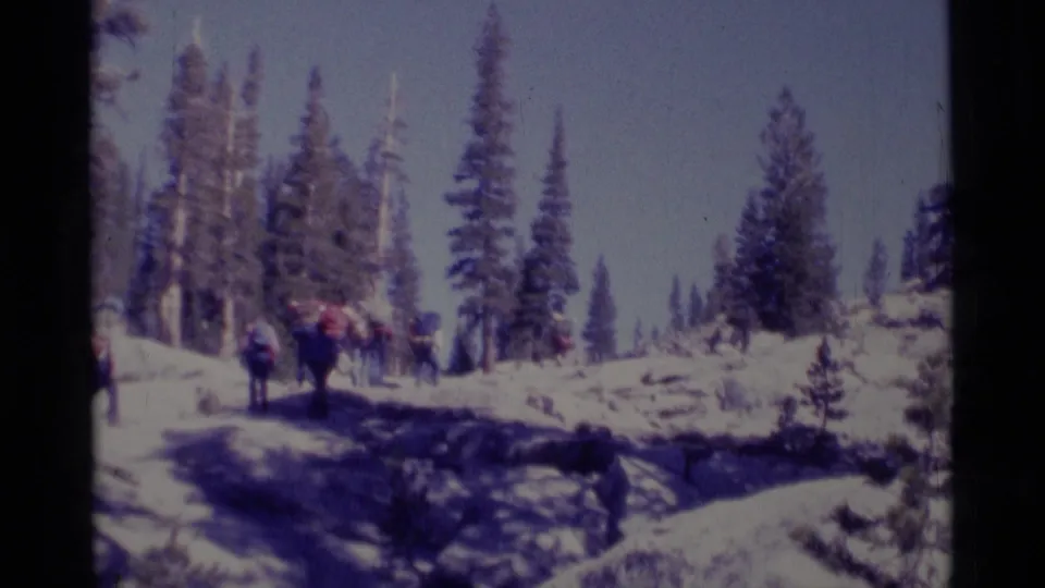 Wide 8mm view of backpackers following a snowy trail through conifers in California's Minaret Wilderness area.