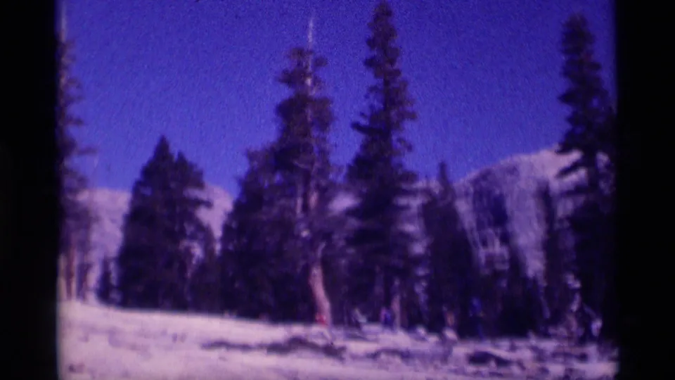 Color-shifted 8mm frame of snow, tall conifers, and distant mountain slopes in the California wilderness setting.