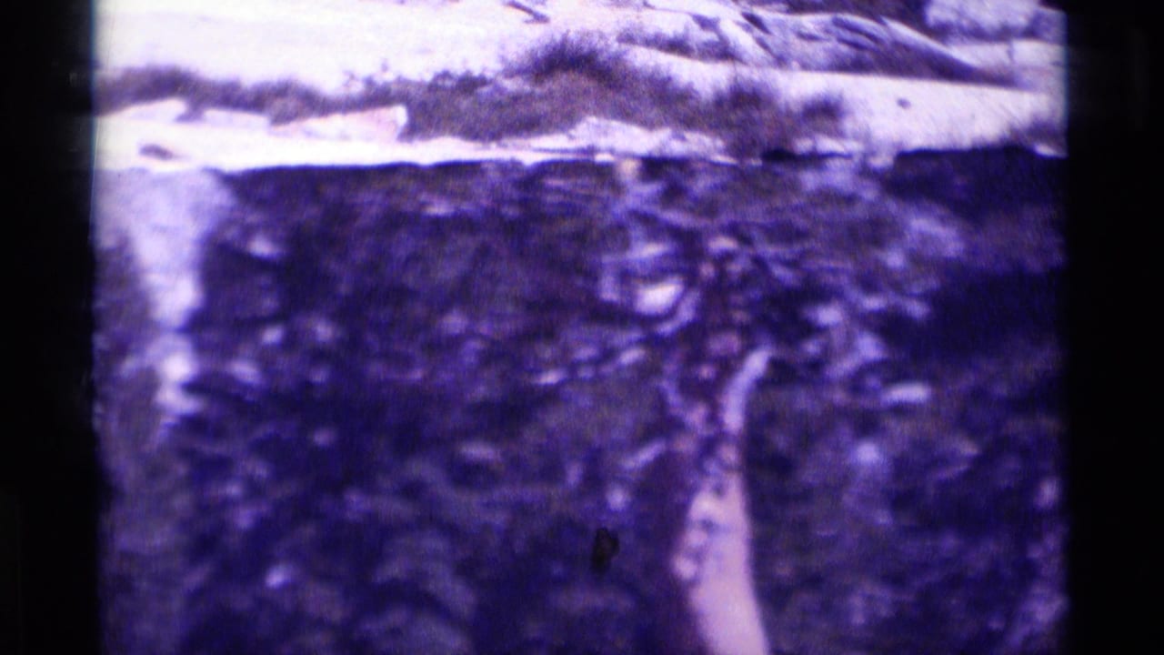1975 8mm frame from Minaret Wilderness showing a soft, purple-shifted rocky alpine view with snow-bright terrain near the top.