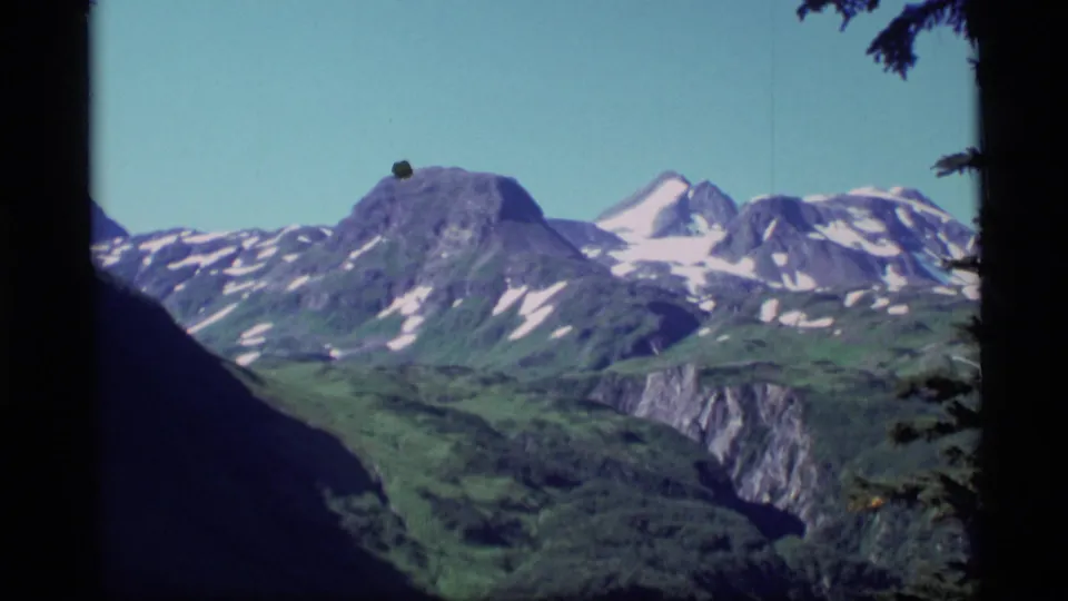 1977 Alaska 8mm frame showing snow-patched peaks and a green valley, with dark frame edges and slight handheld composition.